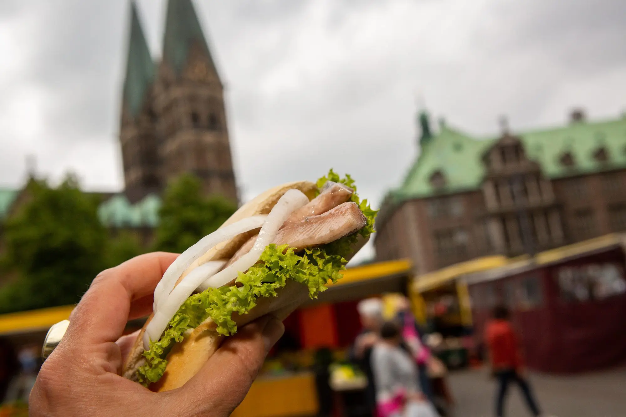 Matjesbrötchen wird in der Hand gehalten; im Hintergrund ist der Bremer Dom zu sehen.