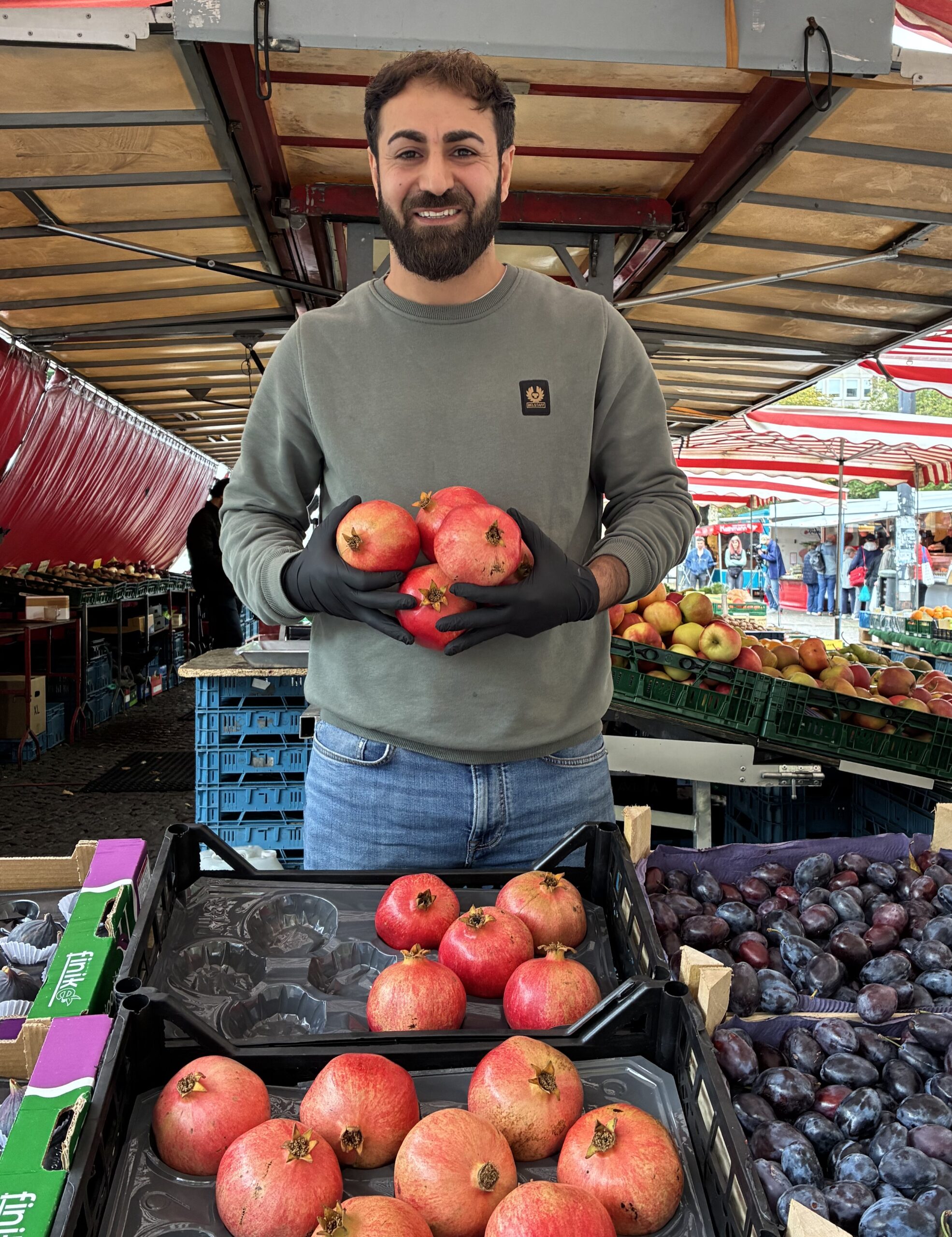 Emre Kaya steht mit einer Handvoll Granatäpfeln an seinem Wochenmarktstand am Domshof