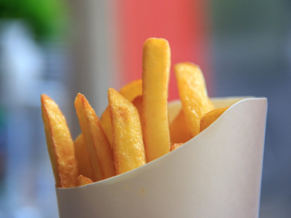 Eine Nahaufnahme von goldenen, knusprigen Pommes frites, die in einer weißen Papiertüte serviert werden, mit einem unscharfen Hintergrund.